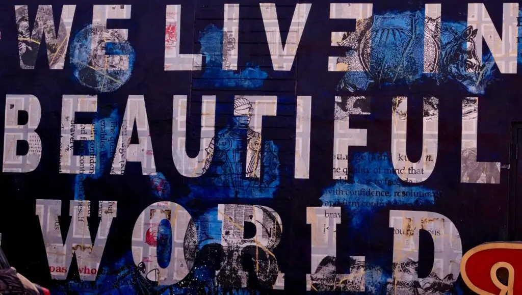 Blue and black mixed-media mural reading "We live in a beautiful world" over collaged newspaper text.