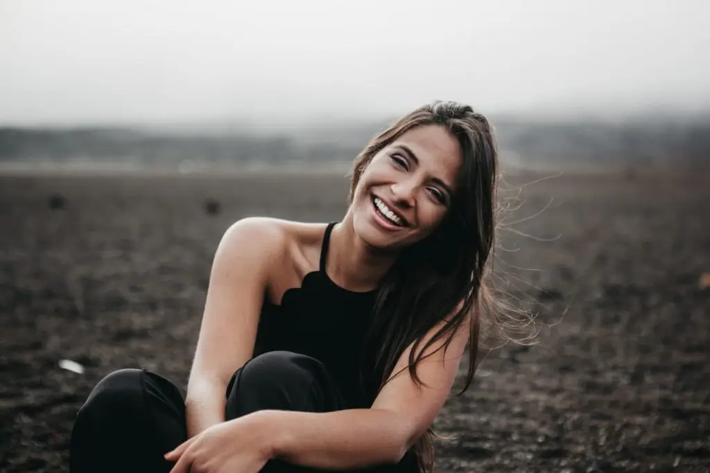 Smiling woman with long brown hair sitting outdoors in a black top, looking happy and at peace.